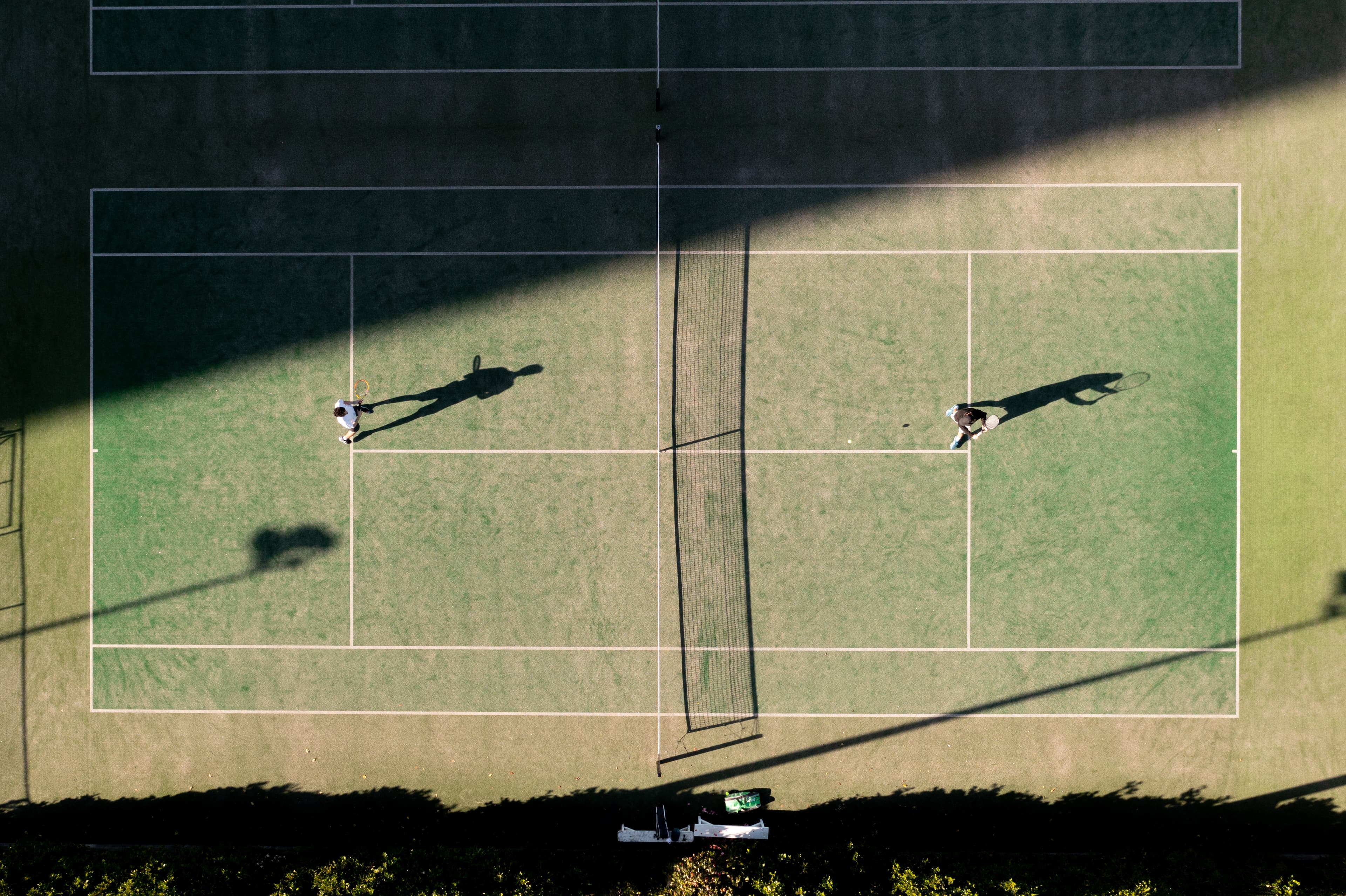 Two tennis players hitting on an outdoor court, viewed from above.